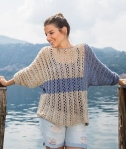 Woman wearing knitted silk/linen blend sweater with all over lace majority of the sweater is a stone colour, but the sleeve and a horizontal stripe across the centre of the body are worked in a contrasting blue grey shade.