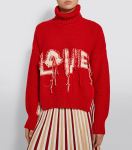 Woman wearing red, roll-neck, knitted sweater with ‘love’ slogan. The sweater fabric appears to be inside out, with the reverse side of knitting and intarsia lettering exposed and the ends still dangling from the intarsia colour-work.