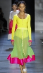 Model wearing bright yellow, scoop neck, knitted cardigan with contrast cuffs in hot pink. Worn with midi length, see through skirt in pale green with hot pink border at hem.