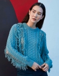 Woman wearing blue knitted sweater with cabled panels and distressed appearance with panels along sides of sweater and sleeves which appear to be ripped open and held only by horizontal threads, with fringe running along these sections.