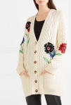 Model wearing cream, oversized, knitted cardigan from REDValentino. There is an all-over cable, textured design and embroidered red, black and blue flower details.