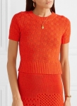 Woman wearing bright orange, short, fitted, knitted top with all-over, chequerboard texture and deep ribbing at hem.