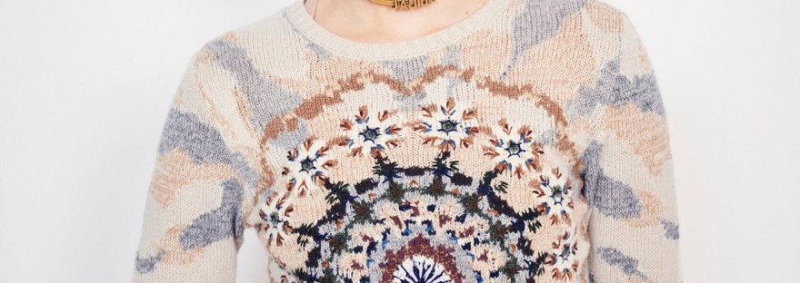 Model wearing Dior summer 2019 collection, including sweater in soft peach, blue and navy colours forming an abstract, kaleidoscope design in intarsia colour-work with embroidery details.
