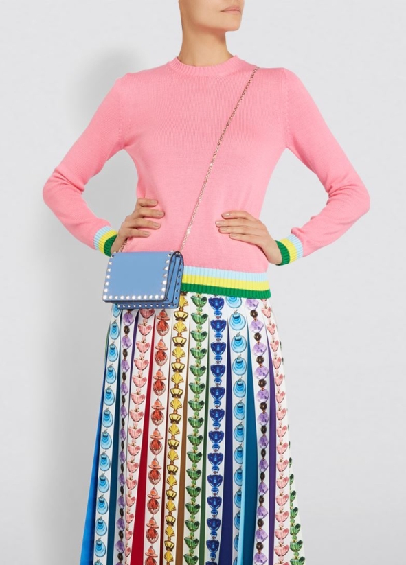 Model wearing knitted, pink sweater with contrasting, green, yellow and blue stripes at cuffs and hem. Worn with multi coloured print, maxi skirt. From Mary Katrantzou, Summer 2019.