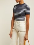 Woman wearing short-sleeved top with crew neck in navy striped with white, made from a stretchy knitted fabric. Worn tucked in to flared white trousers, reminiscent of 1930s daywear.