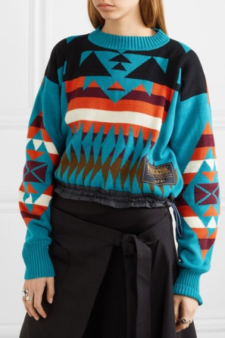 Model wearing knitted jumper with multicoloured, geometric intarsia colour-work design.