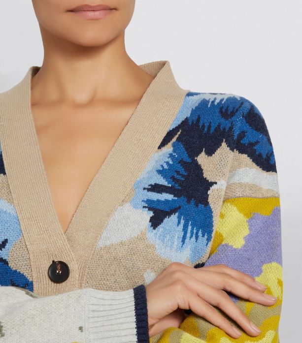 Model wearing knitted, wool cardigan with pale, camel coloured fabric combined with striking, floral intarsia motifs in blues, yellows and greys.