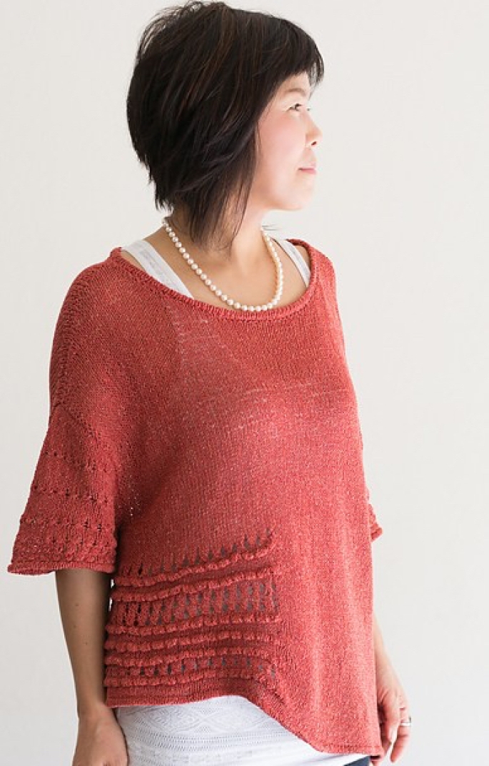 Woman wearing scoop neck, knitted silk/cotton sweater in orange, with dramatic asymmetric hem and textured eyelet sections at sides and bottom of the 3/4 length sleeves.