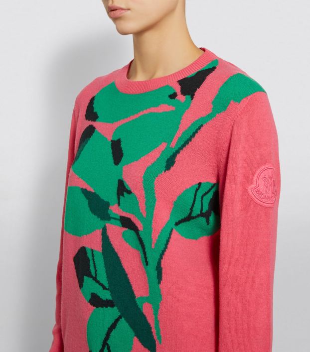 Woman wearing deep pink, knitted sweater with large green, intarsia colour-work motif of a sweep of leaves that covers most of the front.