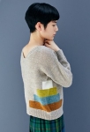 Woman wearing grey, knitted cardigan with multicoloured, rectangle block, intarsia design running across side seams.
