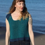 Woman wearing knitted, linen top with short sleeves. Most of the top is in a deep teal shade but the cap sleeves and bottom hem are in a dark blue.