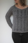 Woman wearing grey, wide scoop neck knitted sweater, with lace columns running vertically across body and sleeves.