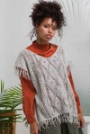 Woman wearing knitted, oversized top with openwork lace and fringe at end of short sleeves and hem.