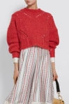 Model wearing a knitted, oversized, cropped red sweater with curving lines of eyelets and voluminous sleeves.