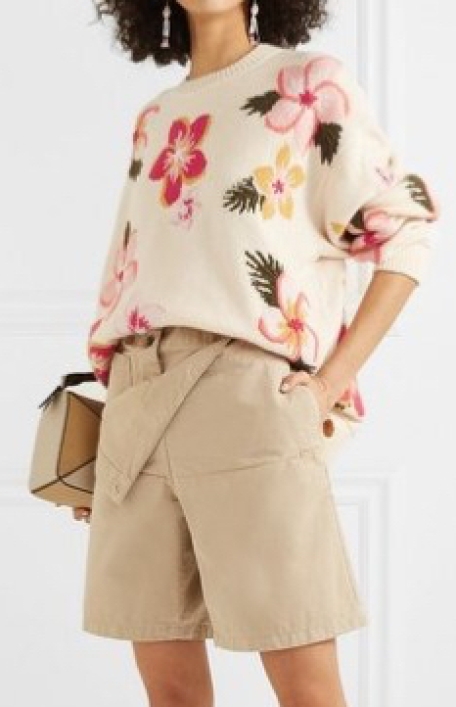 Model wearing oversized, cream sweater with multicoloured floral intarsia design; sweater worn tucked in to stone coloured shorts.