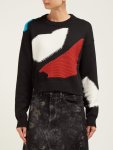 Woman wearing black sweater with geometric intarsia shapes in red, white and blue that give impression of patches.