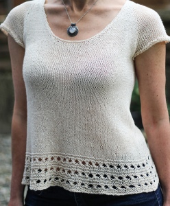 Woman wearing knitted, linen tee with short sleeves, scoop neck and eyelet border at hem.
