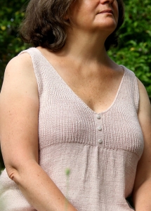 Woman wearing knitted v-neck tank top with rib bodice and button detail, made in wool/cotton.