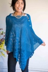 Woman wearing azure blue, knitted silk/cotton poncho, buttoned on one side at shoulder and with wide lace border.