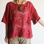 Woman wearing warm red, knitted linen top with wide scoop neck, elbow length sleeves and all-over, twisted stitch and dropped lace pattern.