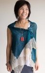 Woman wearing oversized, knitted, cotton vest in teal with cream lace border.