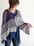 Woman wearing knitted, cotton poncho with patchwork panels of solid, marled and mosaic stitch geometric design.