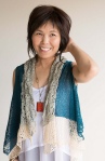Woman wearing oversized, knitted, cotton vest in teal with cream lace border.